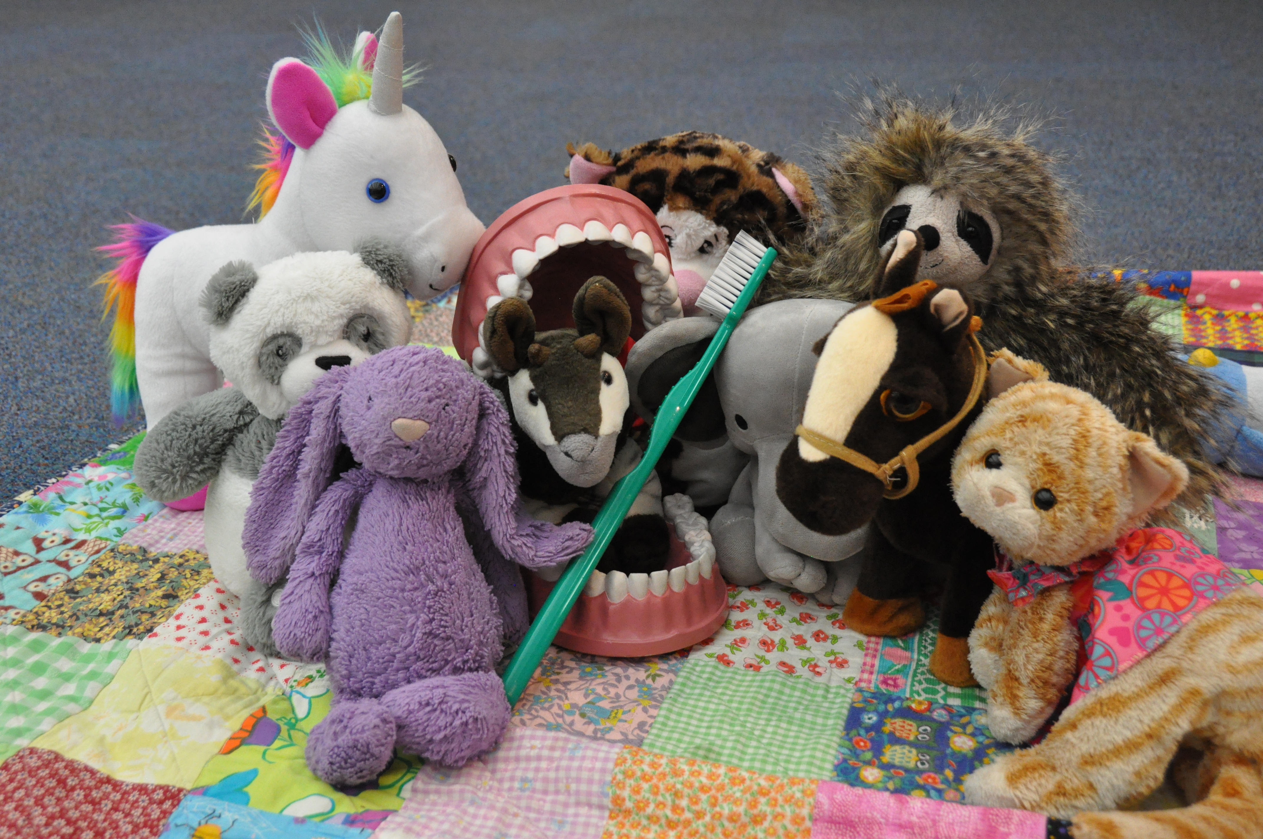 stuffed animals including a unicorn, rabbit, panda and mouse brushing a large set of fake teeth
