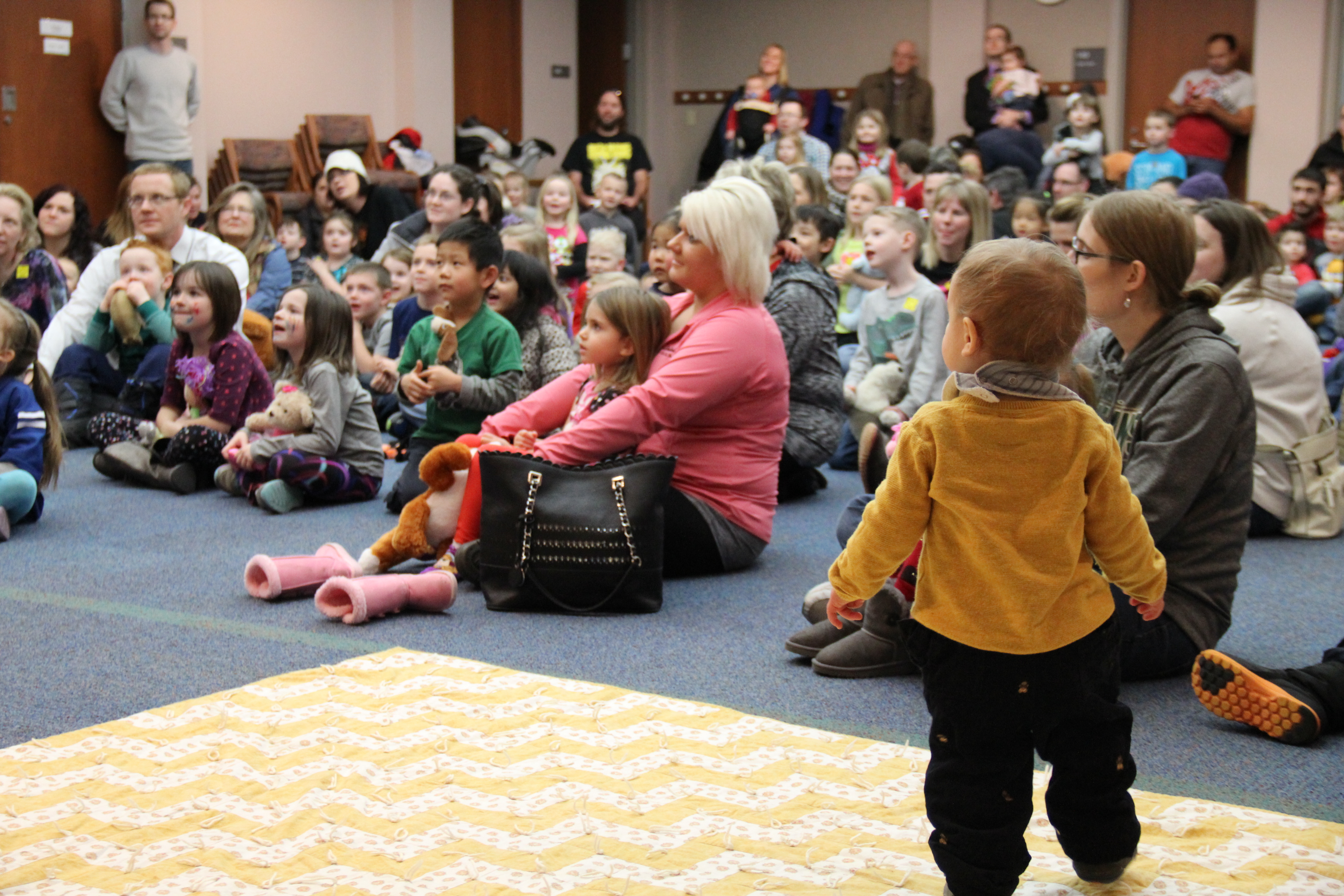 Large room with adults and children watching presenter read. 