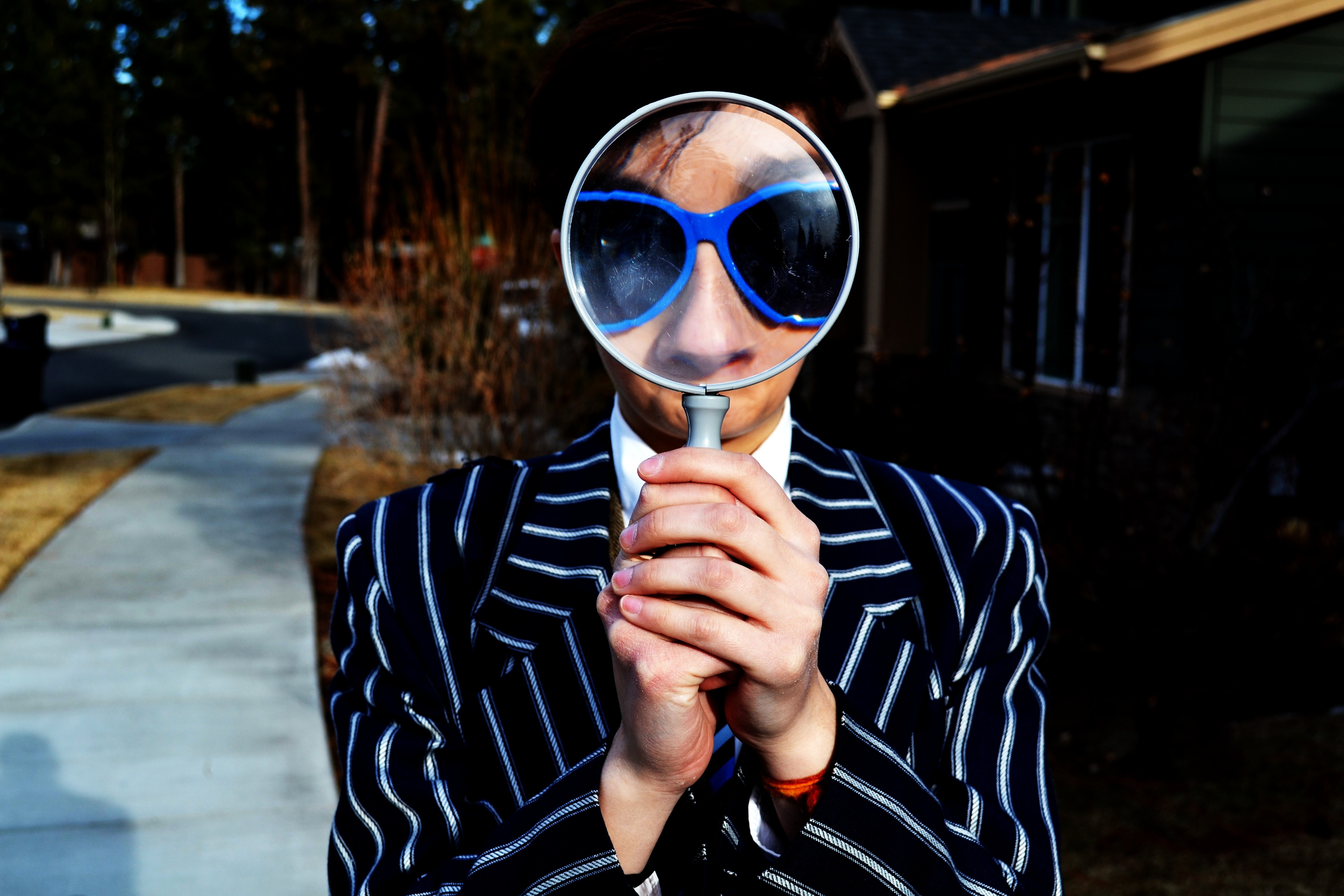 photo of person in suit coat and sunglasses looking through handheld magnifying glass