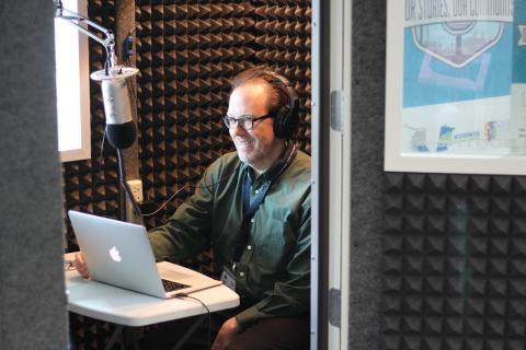 Man sitting in the sound booth with a laptop and microphone