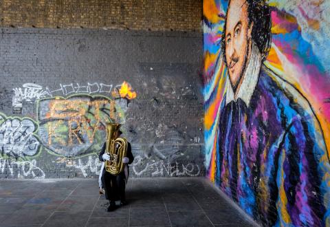 man playing tuba in front of shakespeare mural