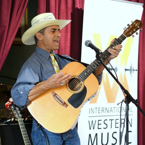 Photo of Kerry Grombacher holding his guitar and singing on stage