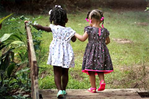 two children holding hands and walking over outdoor bridge