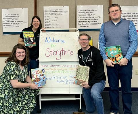 four library staff holding picture books by a "welcome to storytime" sign