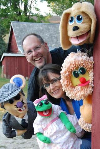 two smiling people surrounded by puppets