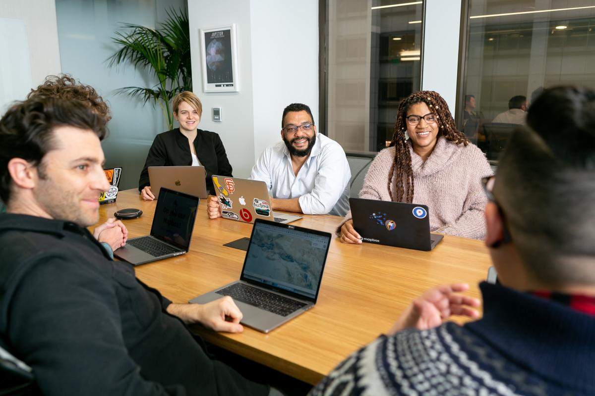 Group of people sitting around a table with their laptops open, happily talking with each other.