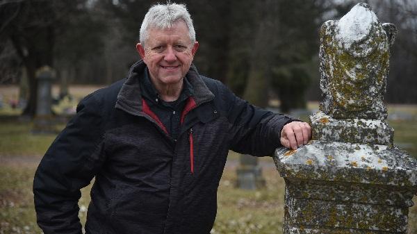 photo of Doug Ohman standing next to a grave monument.