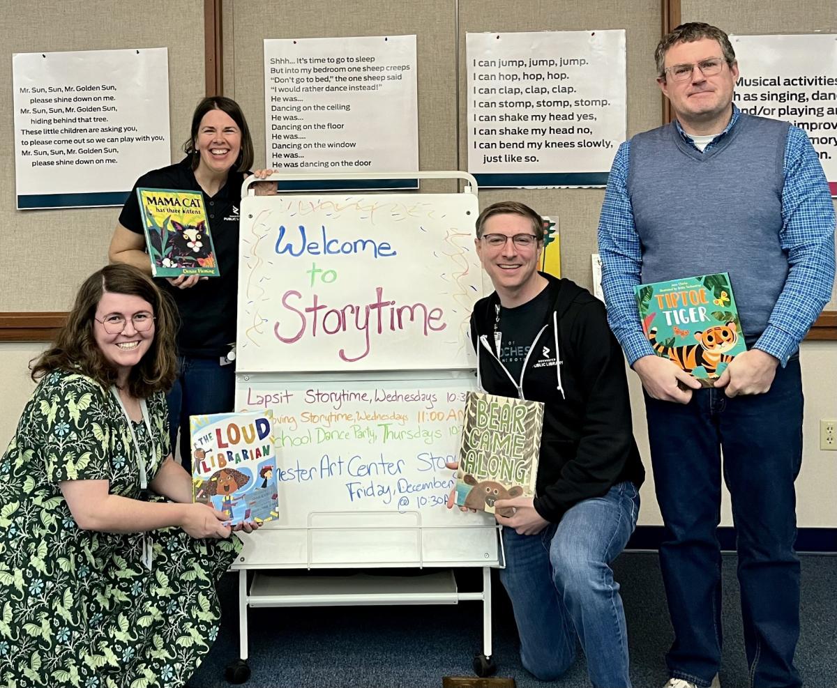 four library staff holding picture books by a "welcome to storytime" sign