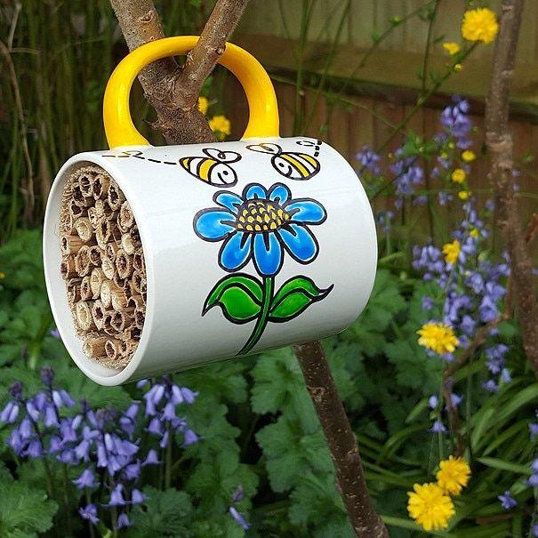 Painted ceramic mug hangs on a branch outside.